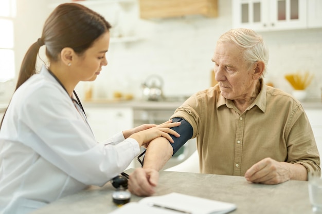 Médico atento se preparando para medir a pressão arterial de um homem idoso
