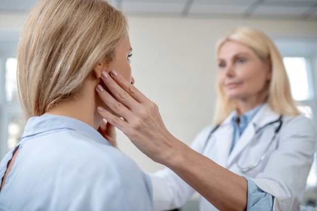 Médico atento tocando con los dedos la cabeza del paciente opuesto y de espaldas a la cámara, realizando un examen