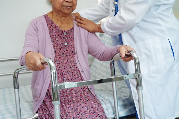 El médico ayuda a una anciana asiática a caminar con un andador en el concepto médico del hospital de enfermería