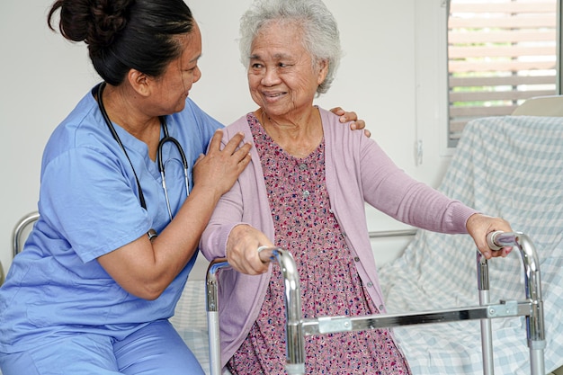 El médico ayuda a una anciana asiática a caminar con un andador en el hospital