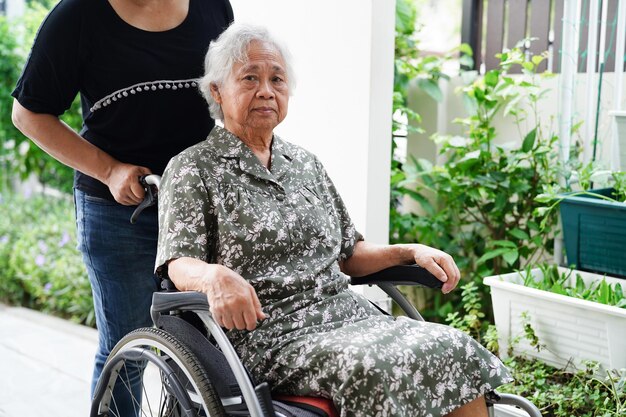 El médico ayuda a una anciana asiática con discapacidad a una paciente sentada en silla de ruedas en el concepto médico del hospital