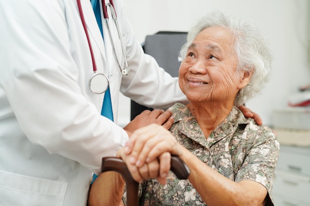 Médico ayuda a una anciana asiática con discapacidad que sostiene un bastón en la mano arrugada en