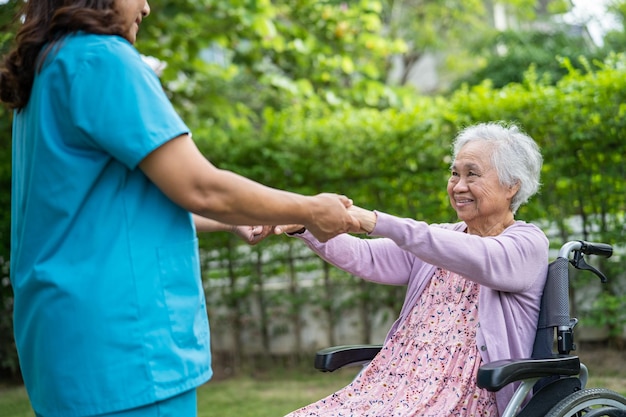 Médico ayuda y cuida a una anciana asiática sentada en silla de ruedas en el parque en la sala del hospital de enfermería concepto médico fuerte y saludable