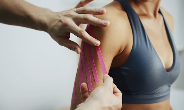 El médico ayuda a la mujer mediante el tratamiento del hombro con cinta de kinesio.