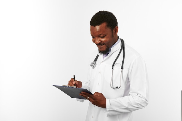 Médico barbudo preto de jaleco branco com estetoscópio preenchendo registros médicos na área de transferência