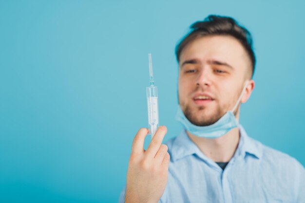 médico barbudo y sosteniendo una jeringa y gritando sobre fondo azul