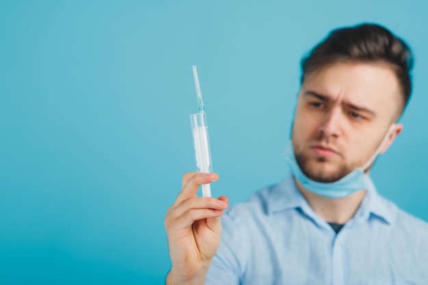 médico barbudo y sosteniendo una jeringa y gritando sobre fondo azul