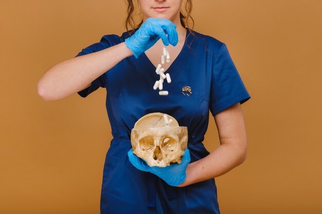 Foto un médico bastante joven vierte cápsulas de vitamina en un cráneo humano. el médico vierte pastillas en el fondo.