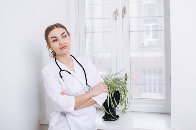 Médico con una bata blanca con un estetoscopio con el telón de fondo de una ventana en una oficina de luz