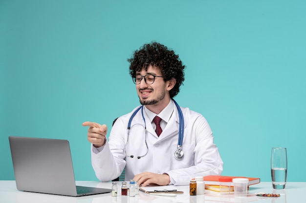 Médico en bata de laboratorio joven médico guapo serio que trabaja en la computadora apuntando a la pantalla