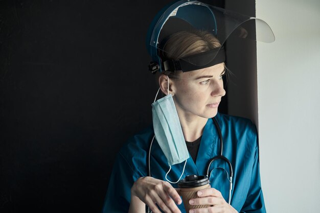 Médico cansado segurando uma xícara de café depois de receber um grande número de pacientes devido à epidemia de coronavírus