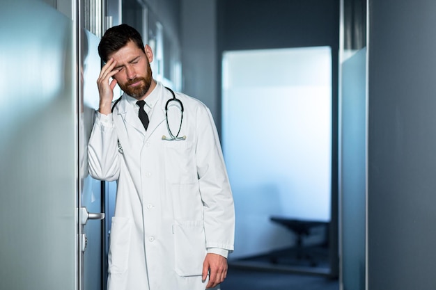 Foto médico cansado sobrecarregado no trabalho tem uma forte dor de cabeça se sente mal um homem no corredor da clínica está desapontado com o resultado