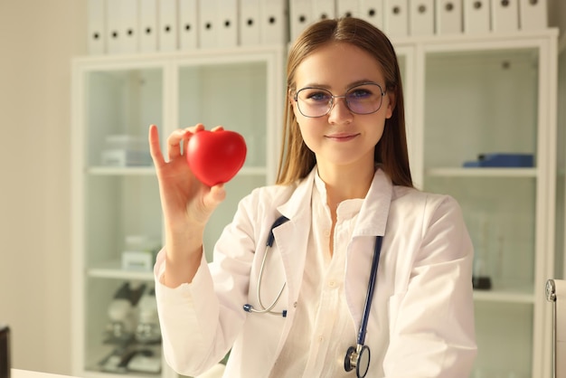 Médico cardiologista segurando coração de brinquedo vermelho no conceito de cuidados de cardiologia clínica