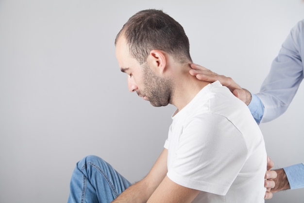 Médico caucásico masajeando el cuello del hombre.