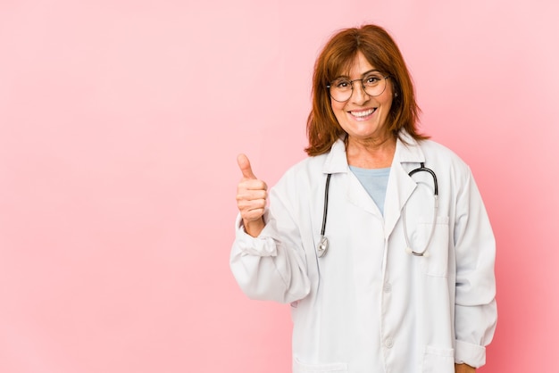 Médico caucásico de mediana edad mujer aislada sonriendo y levantando el pulgar hacia arriba