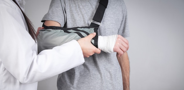 Médico caucásico poniendo cabestrillo en la mano del paciente.