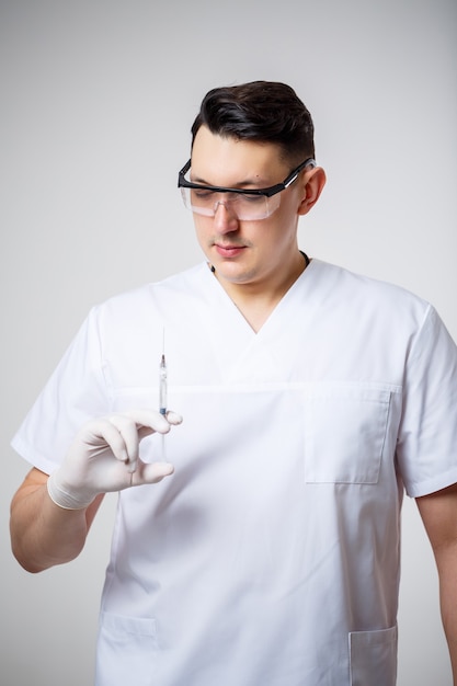 Médico-chefe médico masculino em um terno cirúrgico branco. Retrato de close-up. Possui uma seringa com uma injeção. Isolado em um fundo branco.