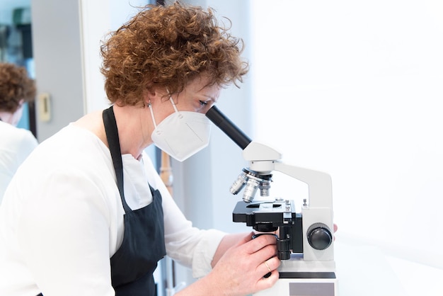 Foto médico cientista analisando amostras em um microscópio com máscara facial durante a pandemia de coronavirus