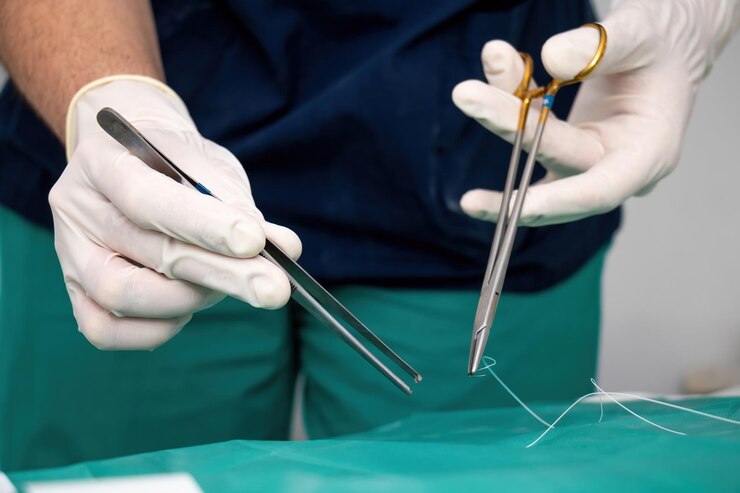 Médico cirujano con guante desechable a mano hacer sutura sujetando fórceps tijera sobre tela verde