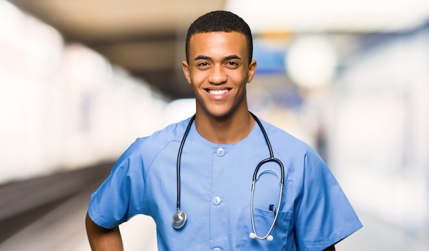 Médico cirujano hombre posando con los brazos en la cadera y sonriendo en un hospital