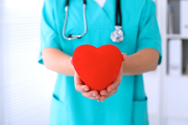 Médico cirurgião feminino com estetoscópio segurando o coração.