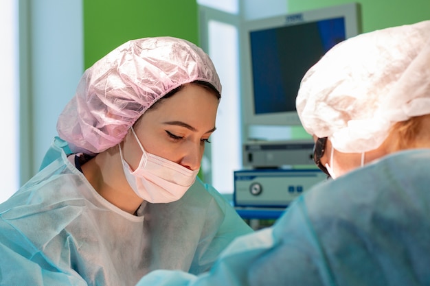 Médico cirurgião feminino ou estagiário usando chapéu e máscara protetora.