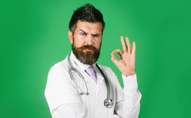 Foto médico cirurgião mostrando o sinal ok com os dedos médico barbudo homem com estetoscópio em casaco branco