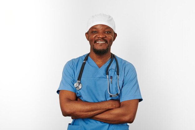 Médico cirurgião negro sorridente homem barbudo de casaco azul e boné médico com estetoscópio de braços cruzados