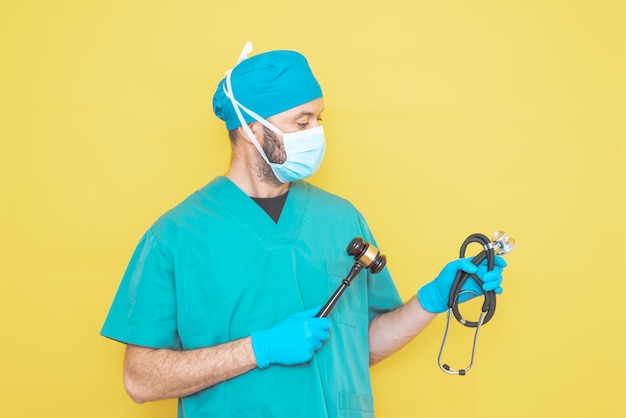 Médico cirurgião vestido com uniforme de sala de operação com estetoscópio em uma mão e martelo do juiz na outra.