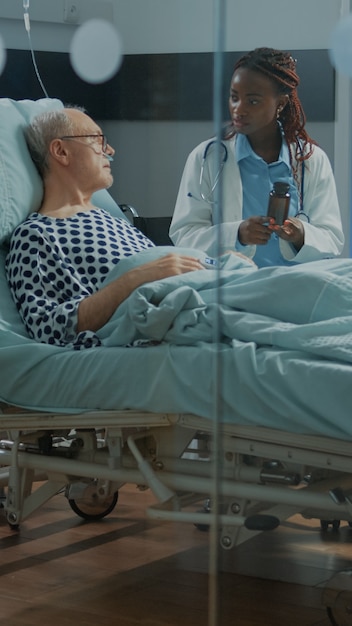 Médico en la clínica dando pastillas al paciente anciano enfermo en la sala del hospital