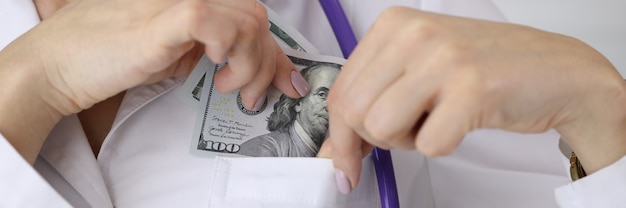 Médico colocando uma nota de um dólar no bolso do uniforme em close da clínica