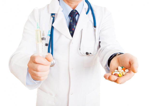 Médico com comprimidos em uma mão e seringas na outra