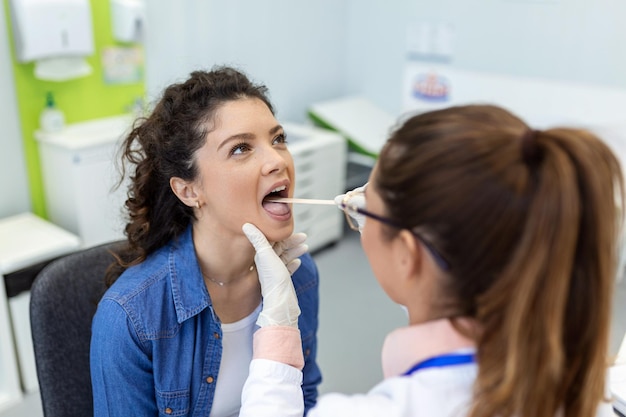 Médico com depressor verificando dor de garganta Médico experiente examina mulher adulta para dor de garganta