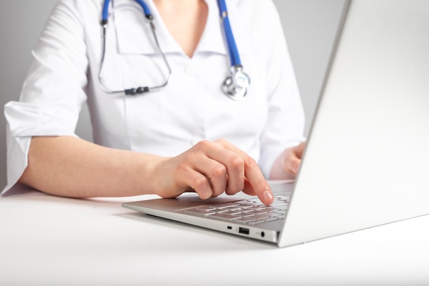 Médico com estetoscópio digitando no teclado do laptop Conceito de saúde e medicina Mulher de jaleco sentado na mesa com computador e prescrevendo medicamentos