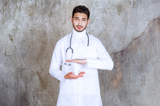 Médico com estetoscópio segurando uma garrafa de desinfetante de mão branca.