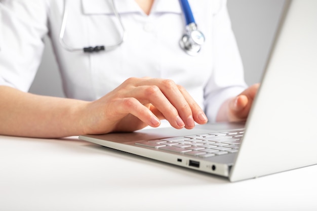 Médico com estetoscópio trabalhando no laptop digitando informações sobre recomendações de diagnóstico do paciente Conceito de saúde e medicina Mulher de jaleco sentado na mesa com o computador