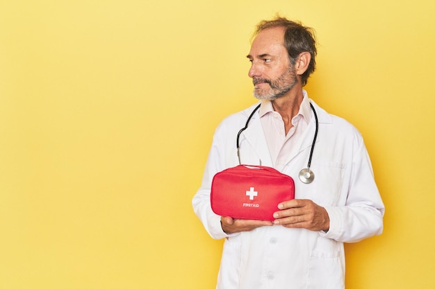 Médico com kit de primeiros socorros em estúdio amarelo