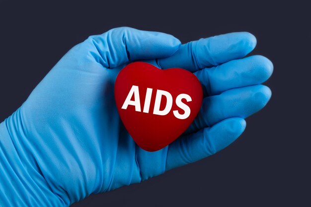 Médico com luvas azuis segura um coração com o texto Síndrome da Imunodeficiência Adquirida com AIDS