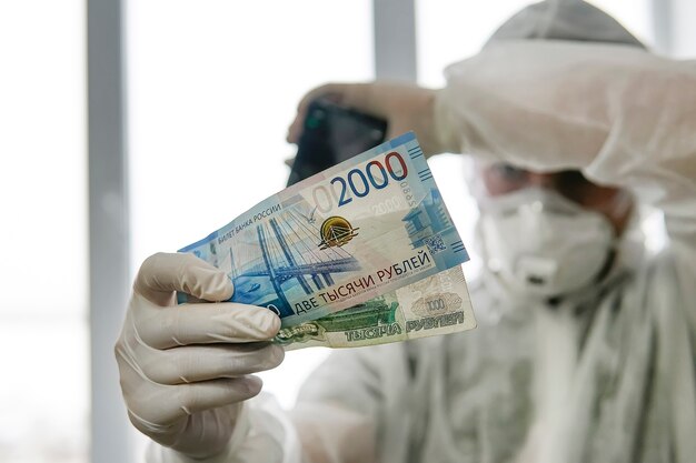 Foto médico com máscara protetora e traje à prova de vírus no hospital conta dinheiro. pagamento a funcionários da zona vermelha. trabalho perigoso com baixo salário. prêmio para médicos que trabalham com pacientes cobiçosos