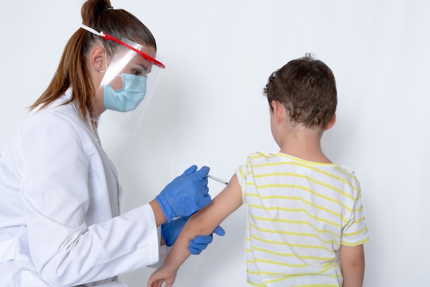 Médico com máscara protetora, inoculando injeção de vacina em menino de cinco anos