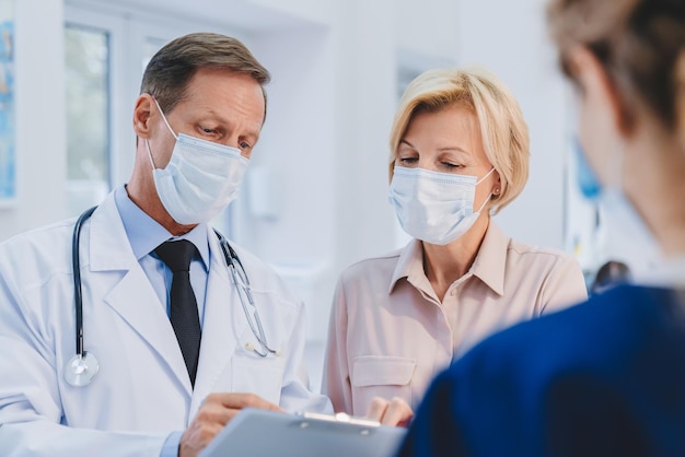 Médico com paciente e recepcionista feminina trabalhando em máscaras de proteção médica no lobby da clínica Conceito de prevenção de epidemias