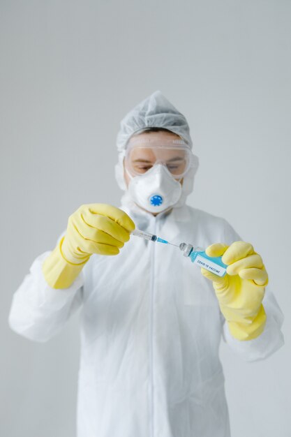 Médico com roupas de proteção segurando a vacina de coronavírus covid-19 azul e olhando para ela, retrato grande