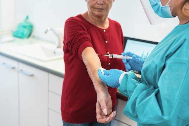 Foto médico com traje de proteção e luvas, dando a um paciente idoso uma vacina para a cura