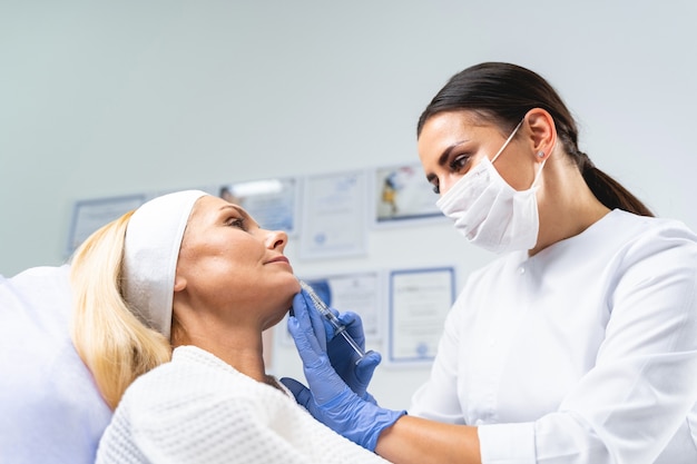 Médico com uma seringa na mão, examinando a pele facial de seus pacientes antes de um procedimento de beleza