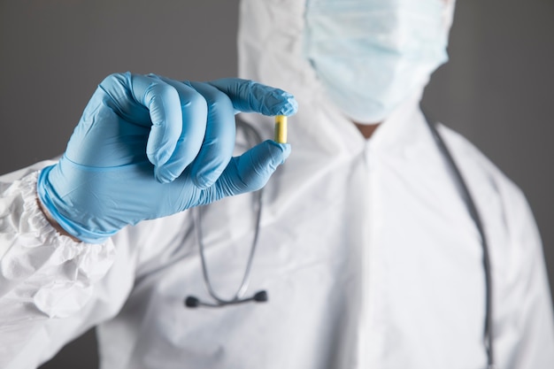 Médico com uniforme de proteção segurando um comprimido em uma cena cinza