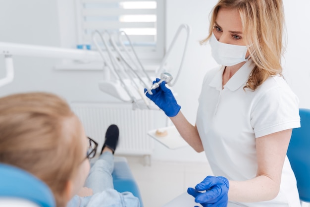 Médico competente e comprometido segurando um dispositivo dentário e se preparando para fazer as meninas sorrirem bonitas