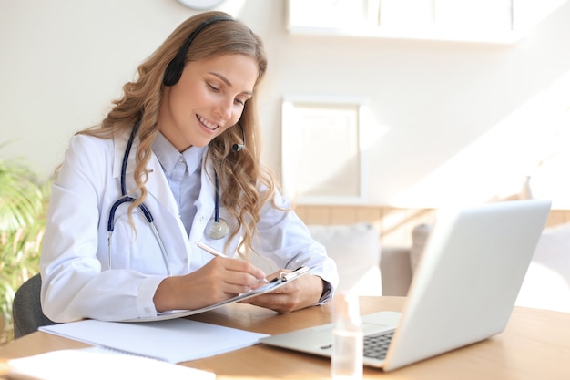 Médico concentrado trabalhando online com um laptop sentado em uma mesa em uma consulta.