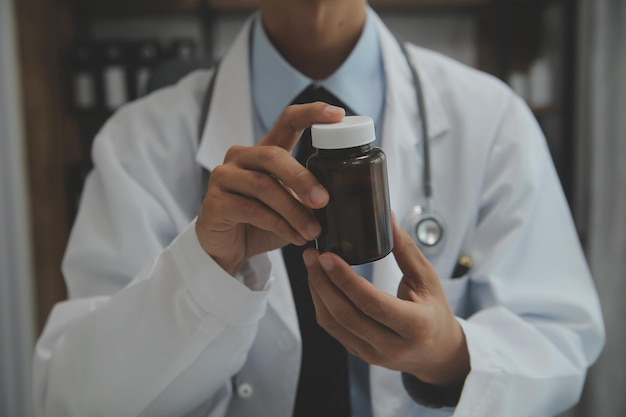 Médico confiante segurando um frasco de comprimidos e escrevendo enquanto conversa com o paciente sênior e revisa sua medicação na sala de escritório