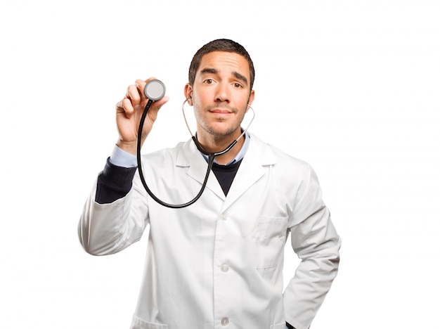 Médico confiante usando um estetoscópio de encontro ao fundo branco