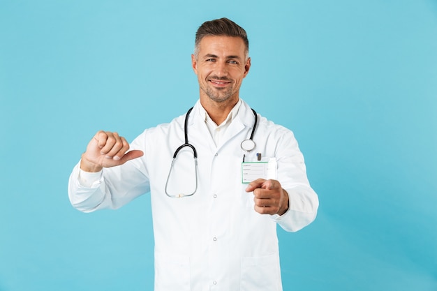 Médico confiante usando uniforme em pé, isolado na parede azul, apontando para si mesmo